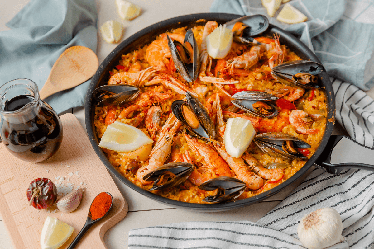 Leckere Paella de Marisco mit Garnelen, Muscheln und Zitronenscheiben, serviert in einer Pfanne.