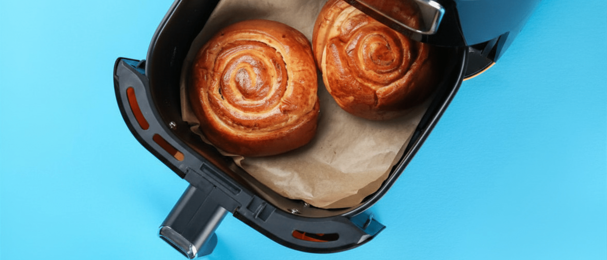 Offener Airfryer-Korb mit auf Backpapier ausgelegten Zimtschnecken.