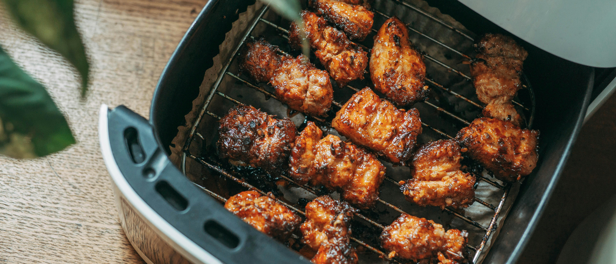 Offener Airfryer-Korb, gefüllt mit Chicken Wings; der Rost ist durch Fett- und Essensreste sichtbar verschmutzt.
